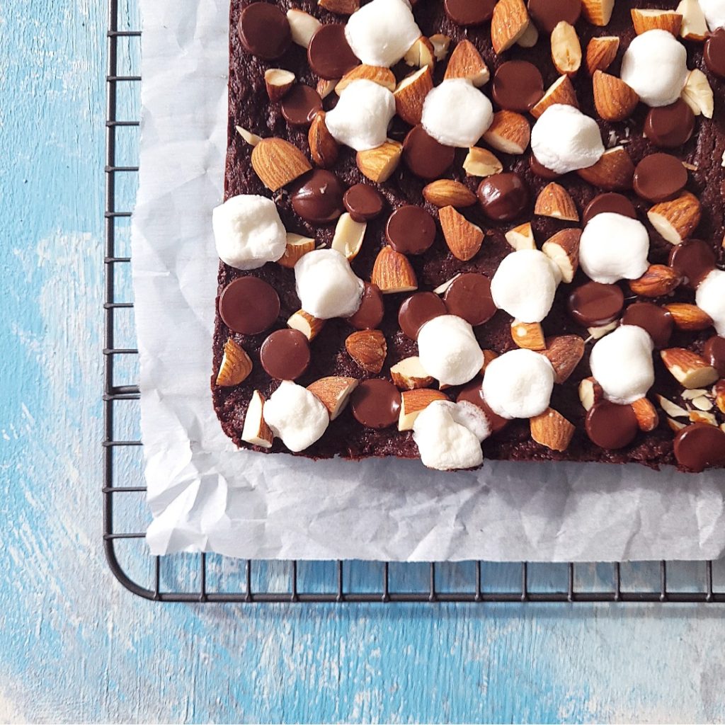 functional image rocky road brownies top down uncut 3 quarter crop on a distressed blue background with a gray baking rack and white parchment paper