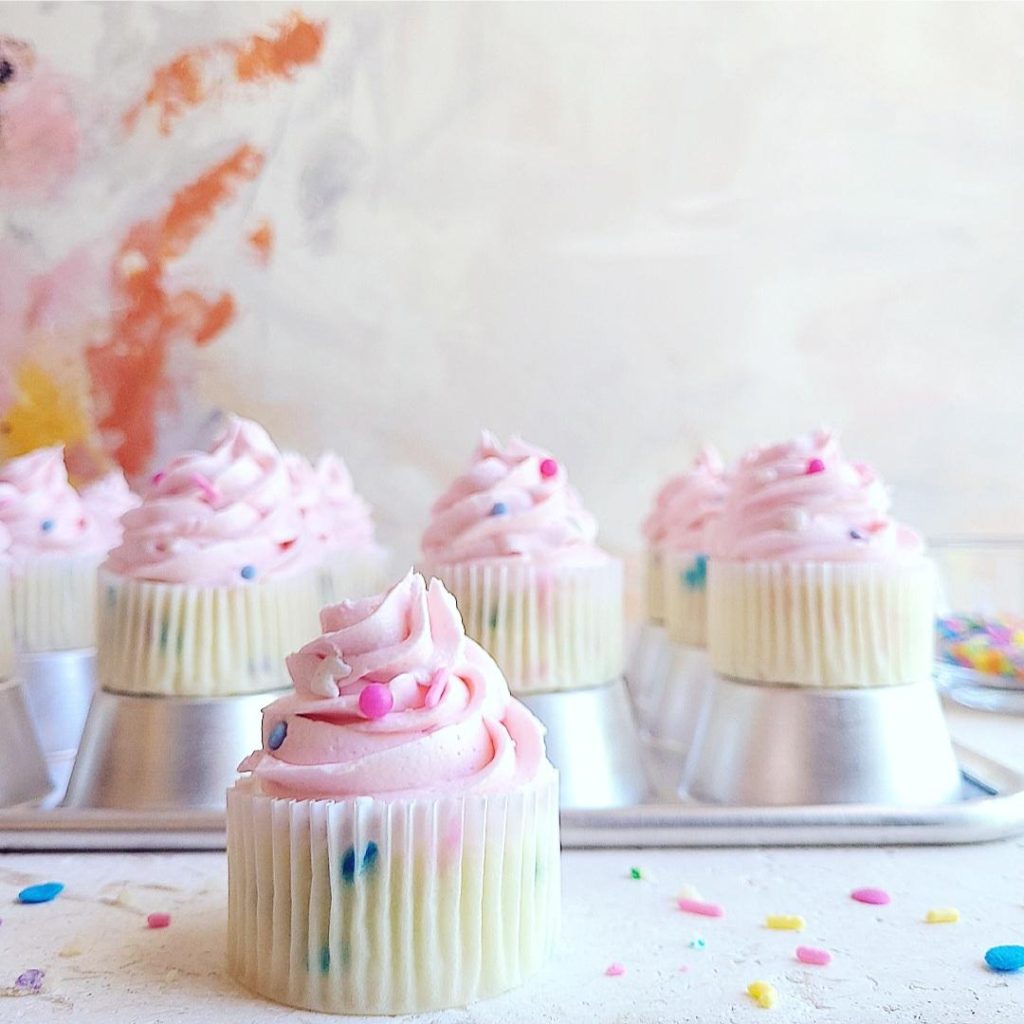functional image confetti sprinkle cupcakes on an upside down shiny aluminum muffin tin iced with pink frosting