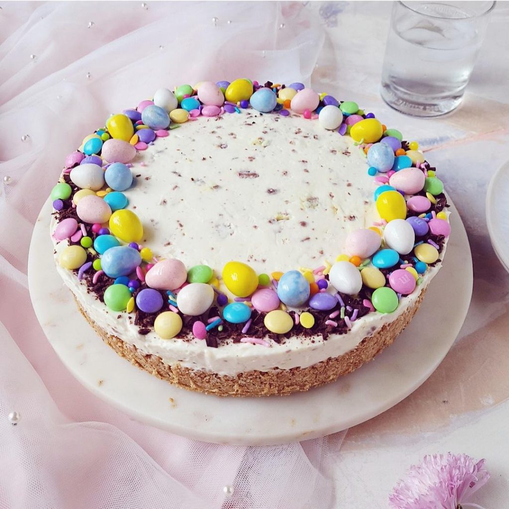 easter cheesecake decorated with cadbury mini eggs, easter m&m's and easter sprinkles uncut on a pink background