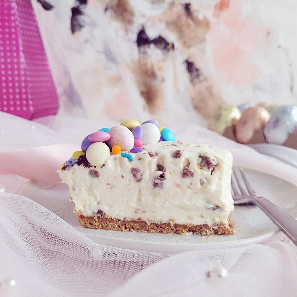 no bake easter cheesecake slice on a plate side view pink abstract background plate is sitting on pink tulle slice decorated with colorful easter candy