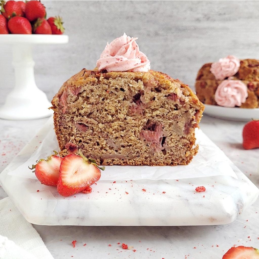 functional image strawberry banana bread side view of loaf cut styled with fresh strawberries and strawberry frosting