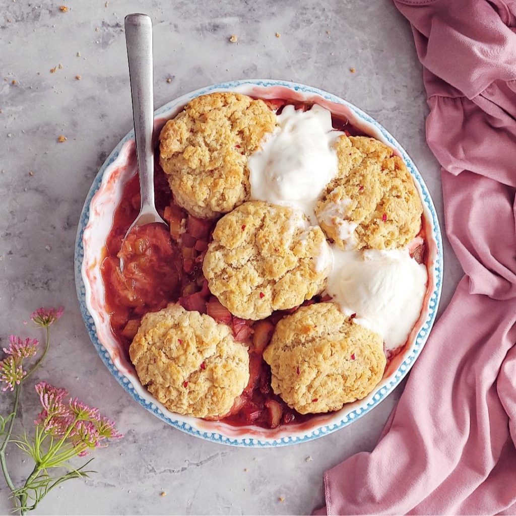 functional image strawberry rhubarb cobbler top down with 2 scoops of ice cream and a spoon in the filling