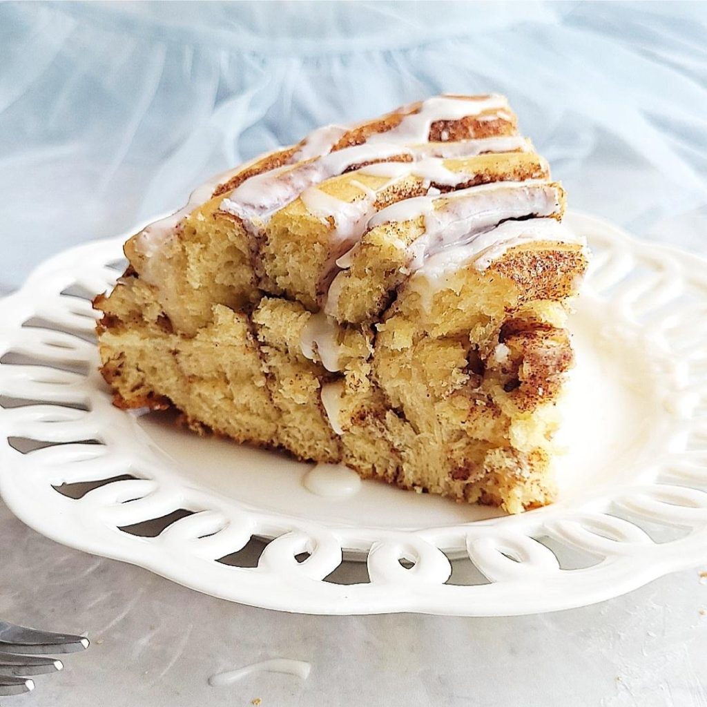 functional image giant cinnamon roll slice on a scalloped white plate with vanilla glaze on top