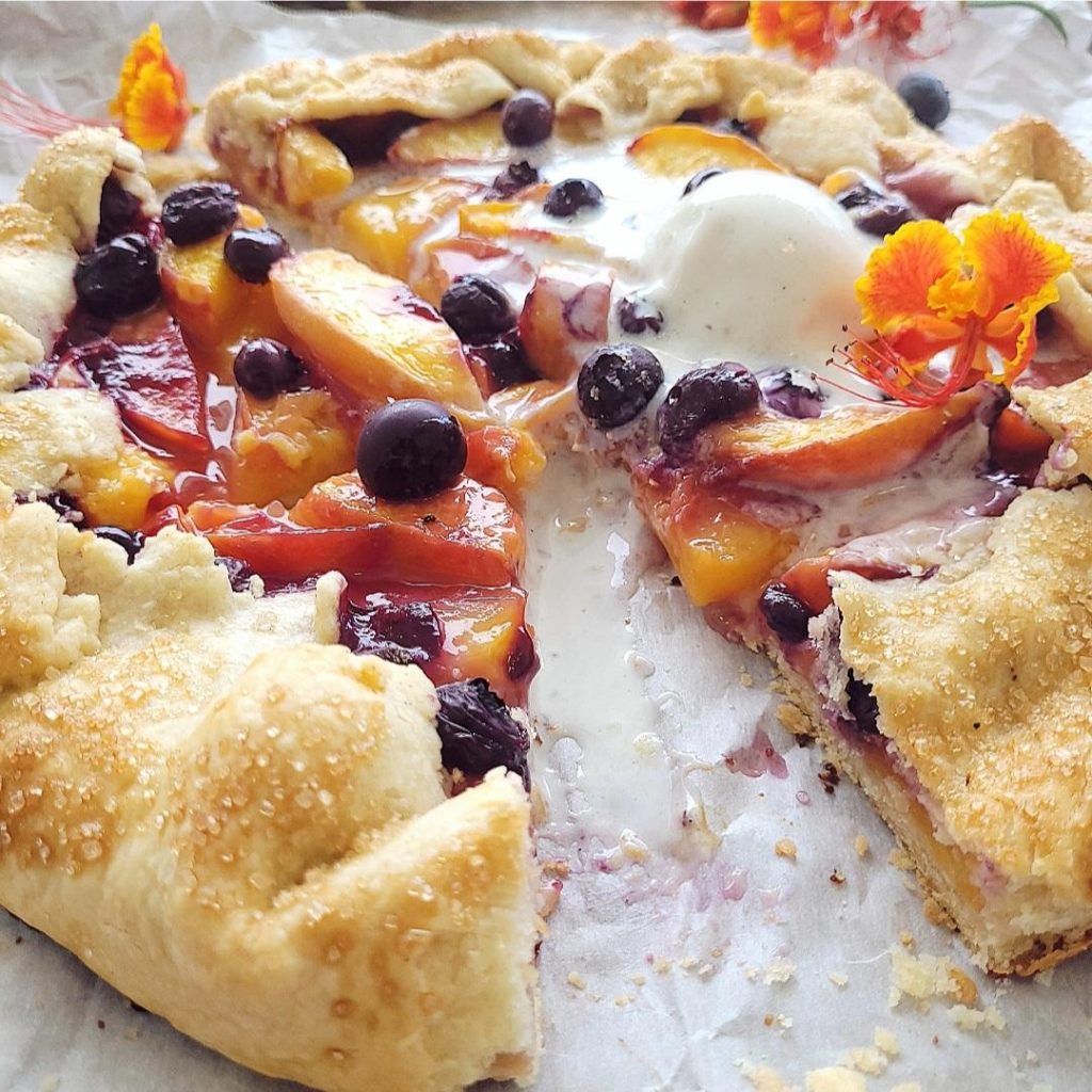 functional image blueberry peach galette close up view with a melting scoop of vanilla ice cream and small orange flowers