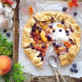 functional image blueberry peach galette rustic pie top down with two slices cut, two spoons and a melting scoop of vanilla ice cream