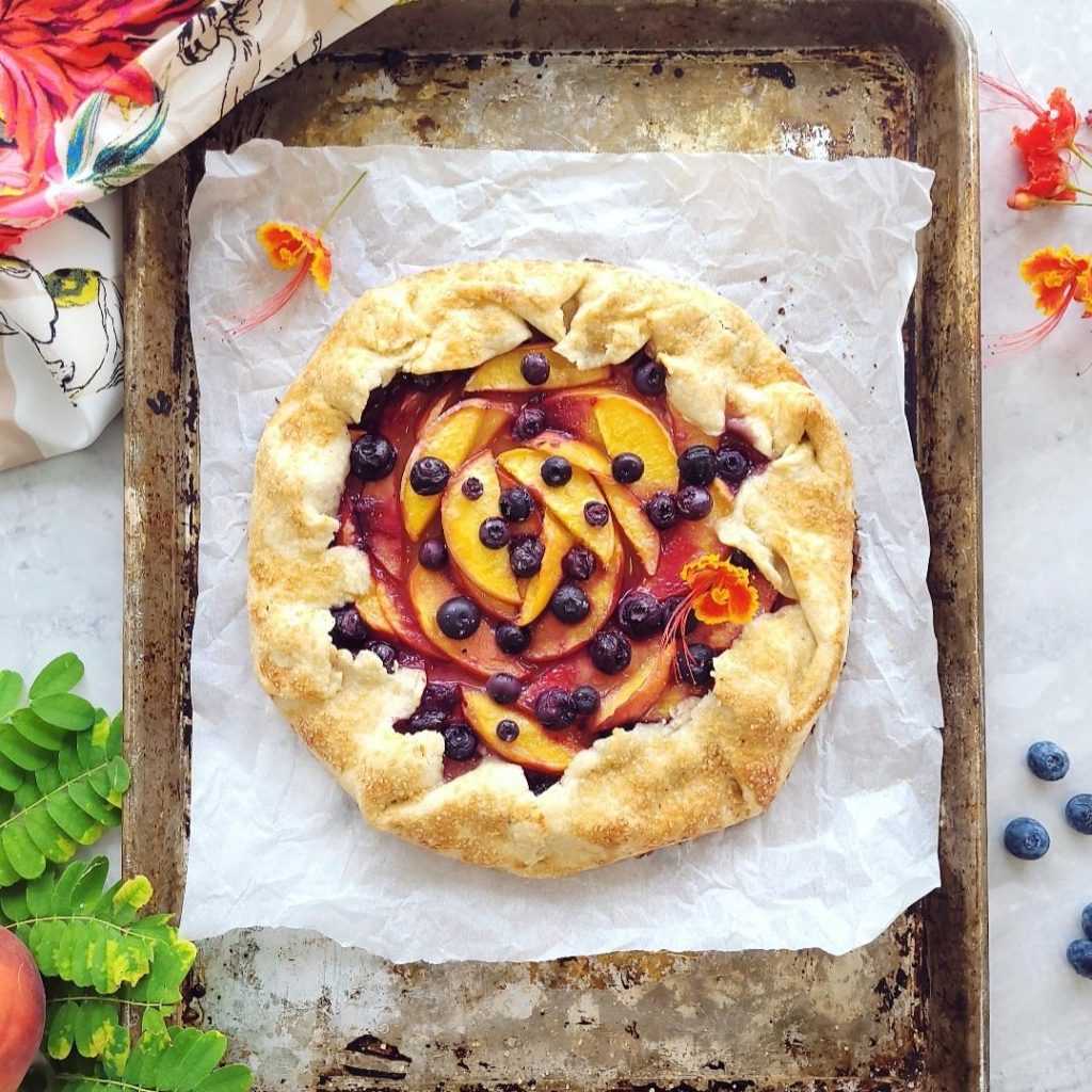 functional image blueberry peach galette top down uncut pit on a cookie sheet with small orange flowers
