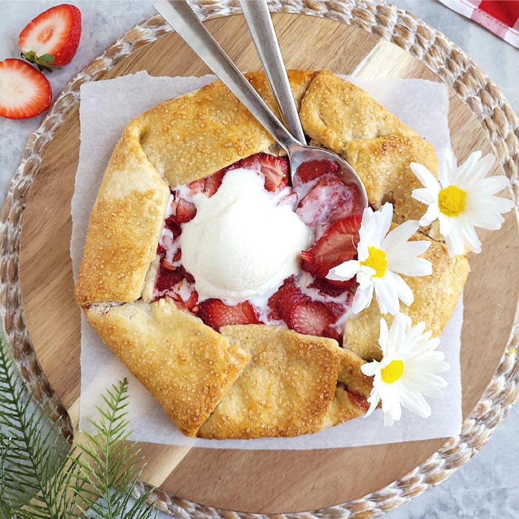 functional image strawberry galette top down with a scoop of ice cream, two spoons and daisy flowers