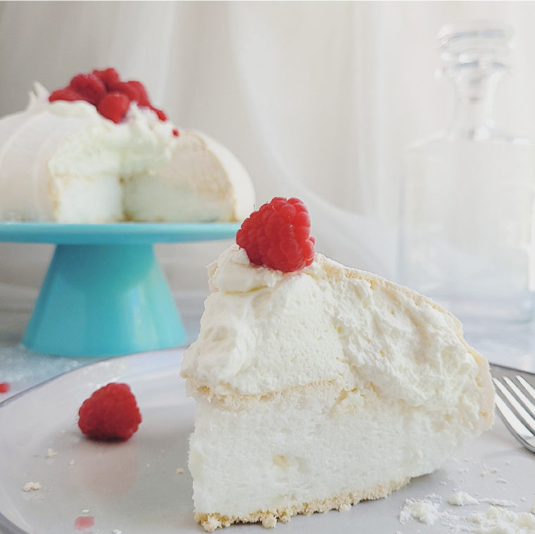pavlova with whipped cream and red raspberries slice on a plate with the remaining cake on a teal blue cake stand in the background