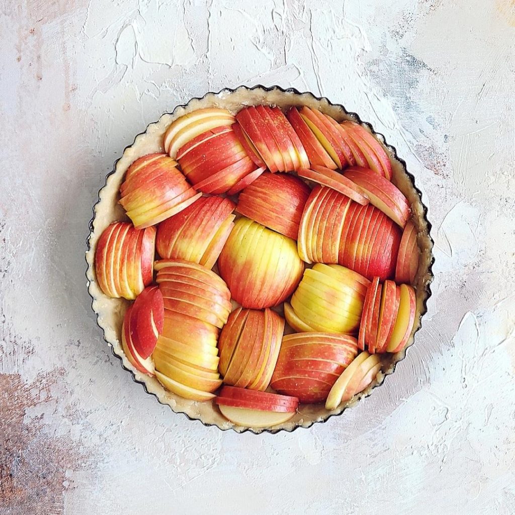 unbaked rustic apple tart stuffed with sliced apples top down on a painted canvas 