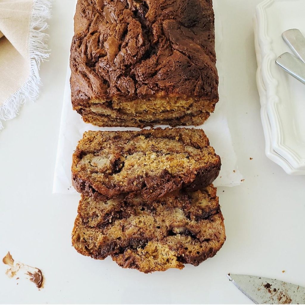 functional image nutella banana bread top down view with two slices cut a dirty knife and white places with scalloped edges