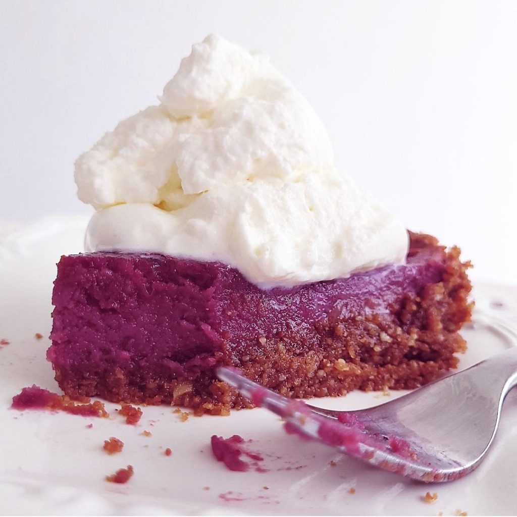 functional image purple sweet potato slice of pie on a white place with whipped cream on top and a fork with purple filling on it from the first bite. 