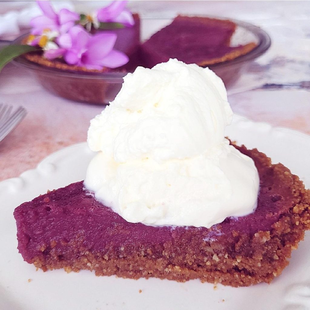 functional image purple sweet potato pie side view to see gingersnap crust filling and whipped cream topping up close pie dish in background
