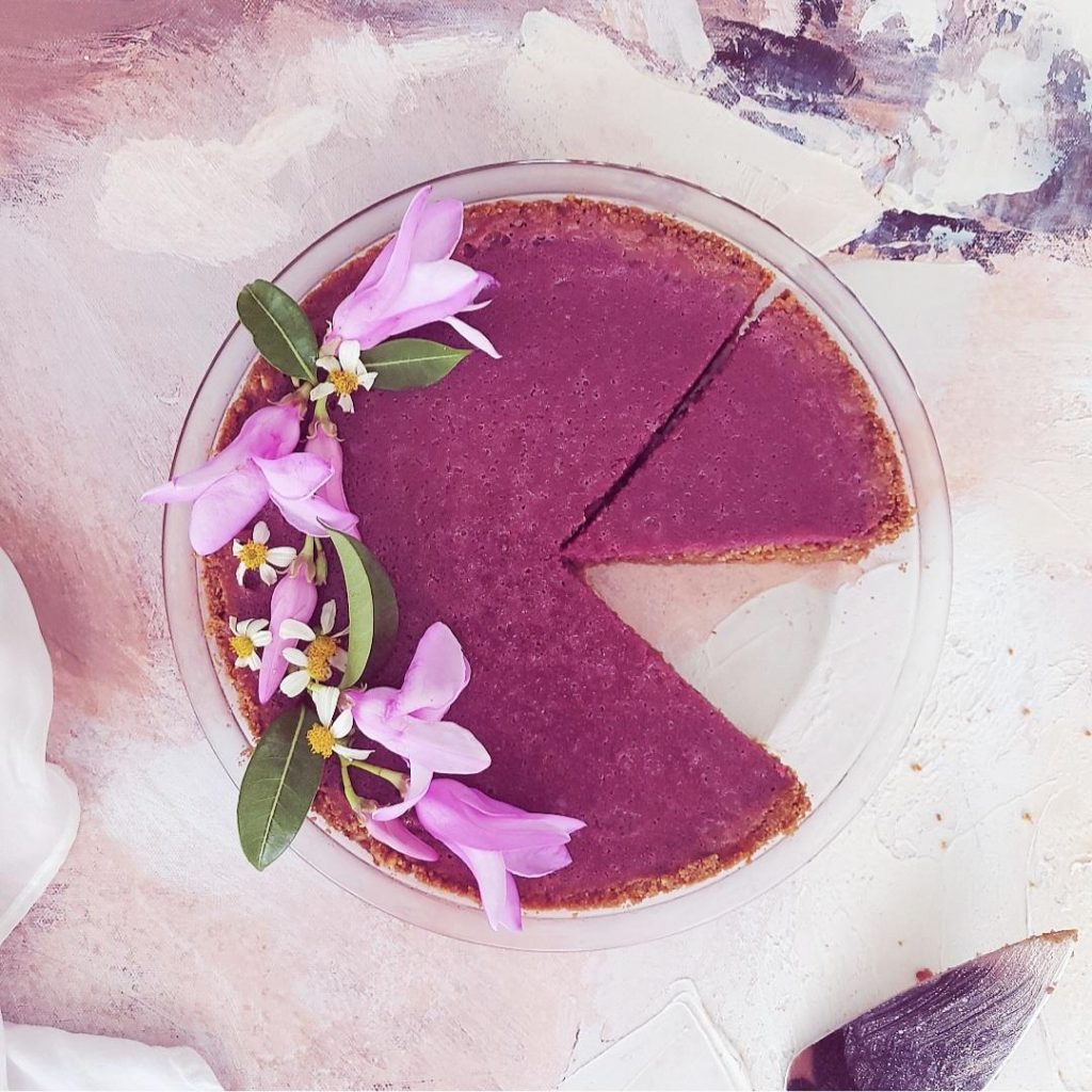 functional image purple sweet potato pie top down with purple flowers one slice missing from the pie place and other slice cut background is abstract canvas