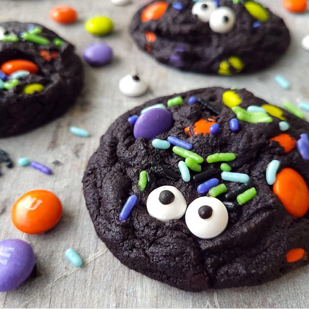 functional image dutch chocolate halloween cookies. black cookies decorated with candy eyeballs, halloween sprinkles and halloween m&m's on a distressed gray surface