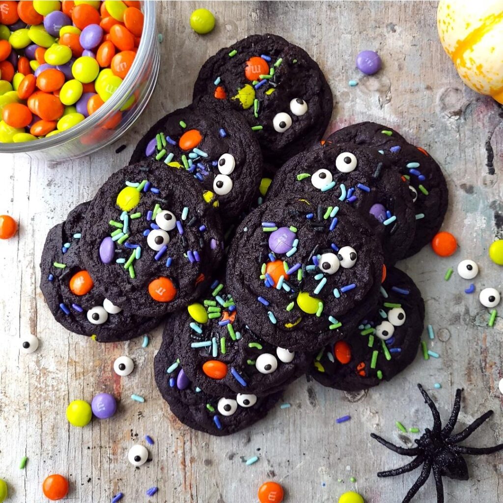 functional image chocolate halloween cookies with m&m's. top down view of cookies with halloween sprinkles and candy eyeballs on a distressed gray background