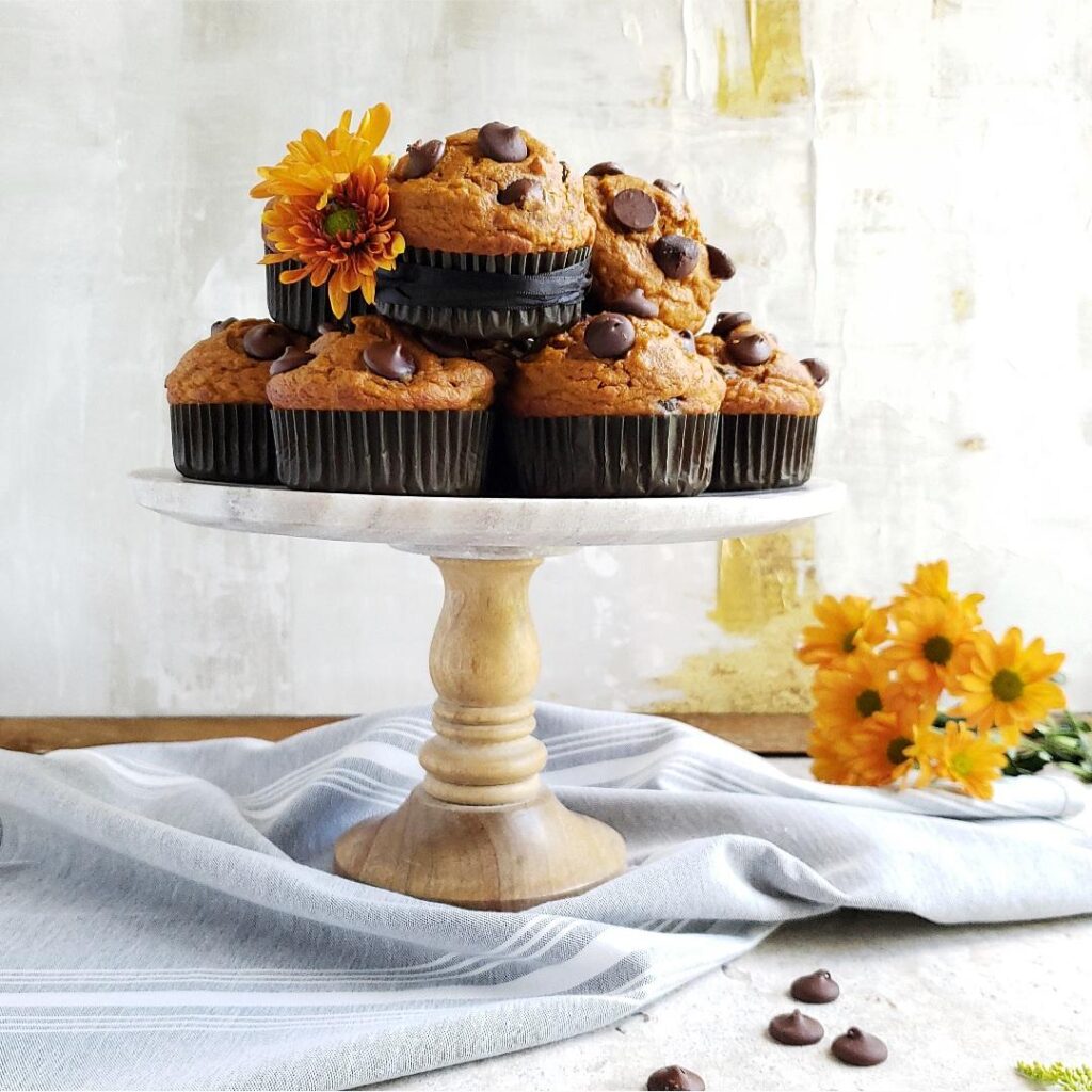 functional image pumpkin chocolate chip muffins piled on a cake stand styled with orange flowers for fall