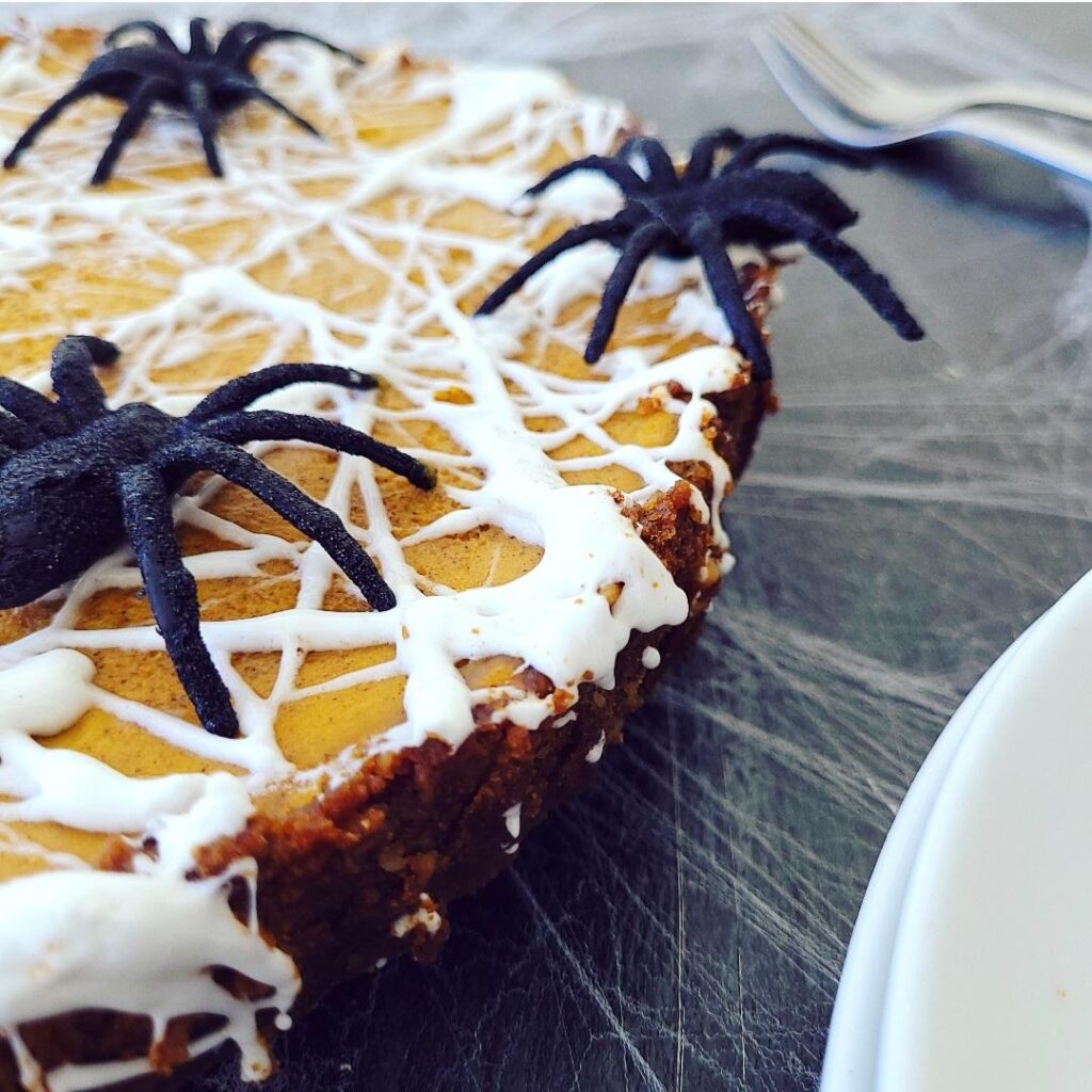 functional image marshmallow spiderweb pumpkin tart spooky halloween dessert with black spiders on top for decoration. shot on a black background zoomed in close up at 3/4 angle