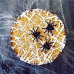 functional image pumpkin tart with melted marshmallow spiderwebs on top top down view with giant black spiders on top. background is black with real cobwebs