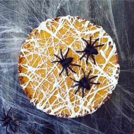 functional image pumpkin tart with melted marshmallow spiderwebs on top top down view with giant black spiders on top. background is black with real cobwebs