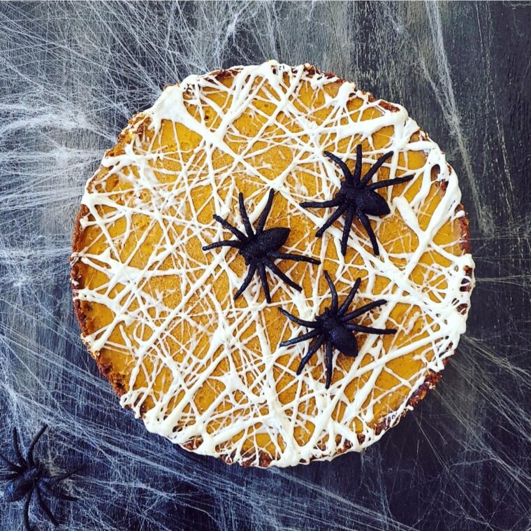 functional image pumpkin tart with melted marshmallow spiderwebs on top top down view with giant black spiders on top. background is black with real cobwebs