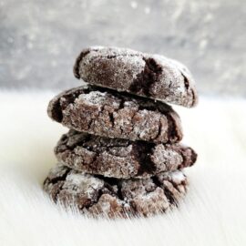 functional image chocolate molasses crinkle cookies side view cookies stacked four high on a snowy surface and a gray wintery background.