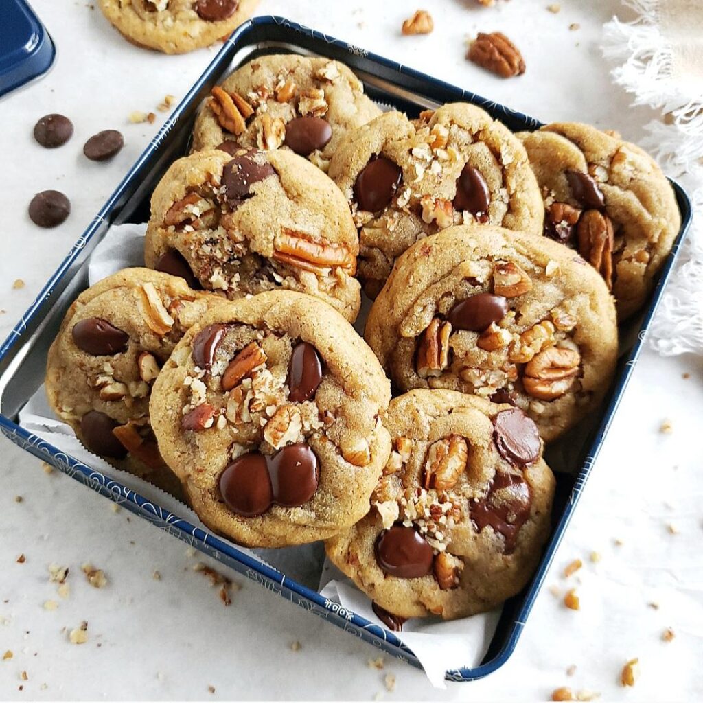 functional image chocolate chip cookies with pecans piled in a square blue cookie tin 