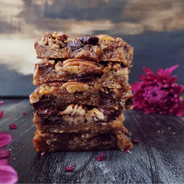 functional image dark chocolate pecan pie bars stacked5 high with purple flowers in the background on a black wood surface