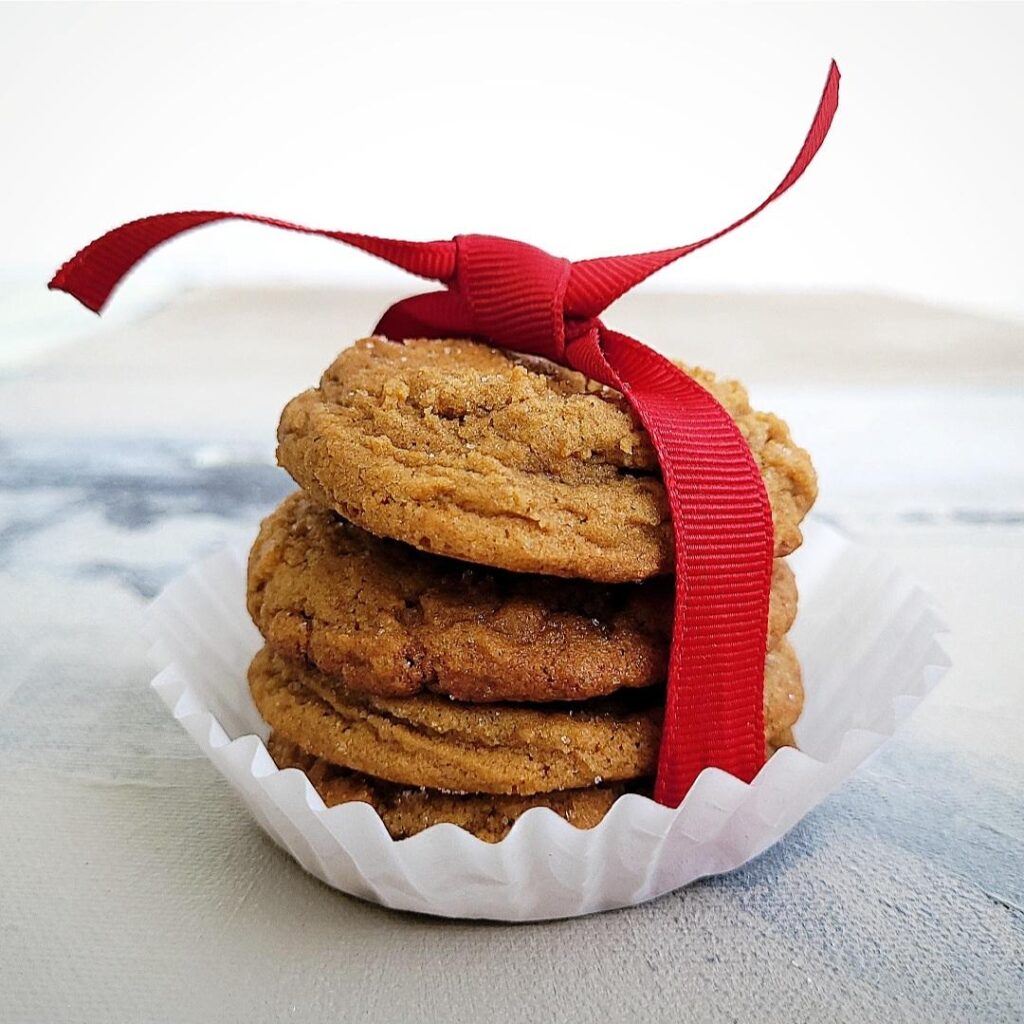 functional image four gingerdoodle cookies stacked in a white cupcake liner and tied with a red ribbon side view on distressed gray backgroun