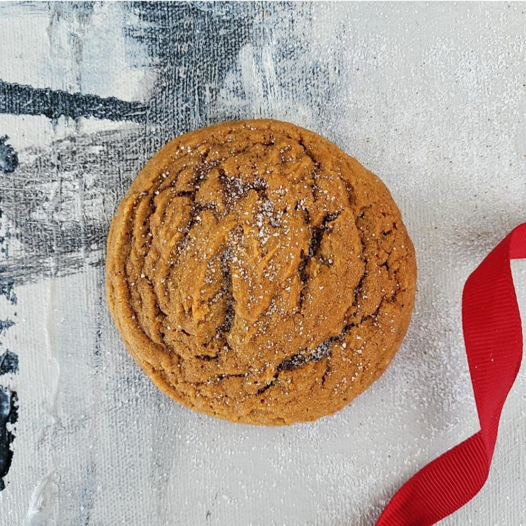 functional image one gingerdoodle cookie top down sprinkled with sugar on a distressed gray background and a red ribbon in lower right corner