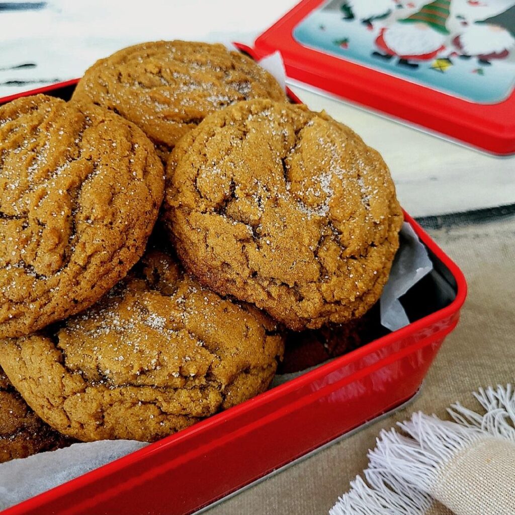 functional image gingerdoodle cookies sprinkled with sugar stacked in a square red cookie tin close up view with the tin's lid in the background