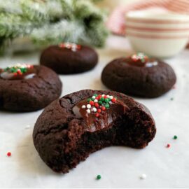 dark chocolate thumbprint cookies four cookies with holiday sprinkles close up view of a bitten cookie holiday greenery in the background