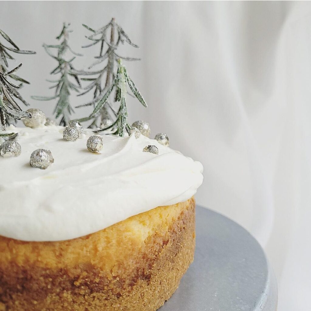 white chocolate christmas cheesecake partial view of cheesecake on left side of frame topped with white chocolate whipped cream rosemary trees and decorative little silver balls