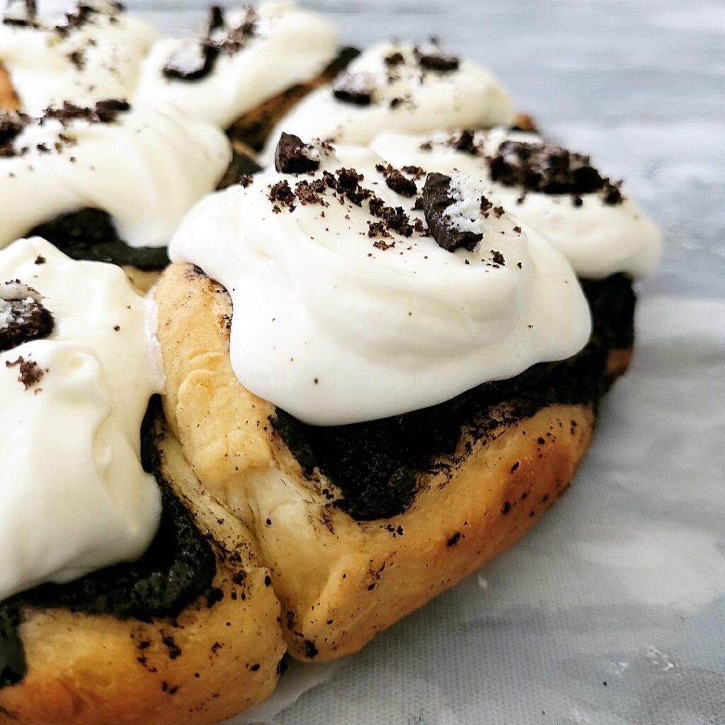 oreo cinnamon rolls close of of rolls with cream cheese icing and oreo cookie crumbs on top rolls are in the circular pattern of their baking pan and are uncut background is gray