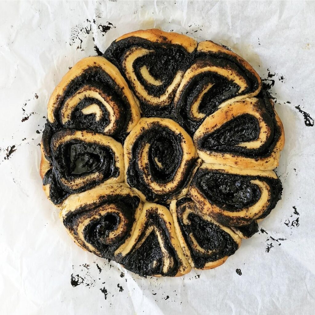 oreo cinnamon rolls top down view of ten baked rolls in the circular shape of the baking pan. rolls are swirled with black cocoa powder background is white parchment paper
