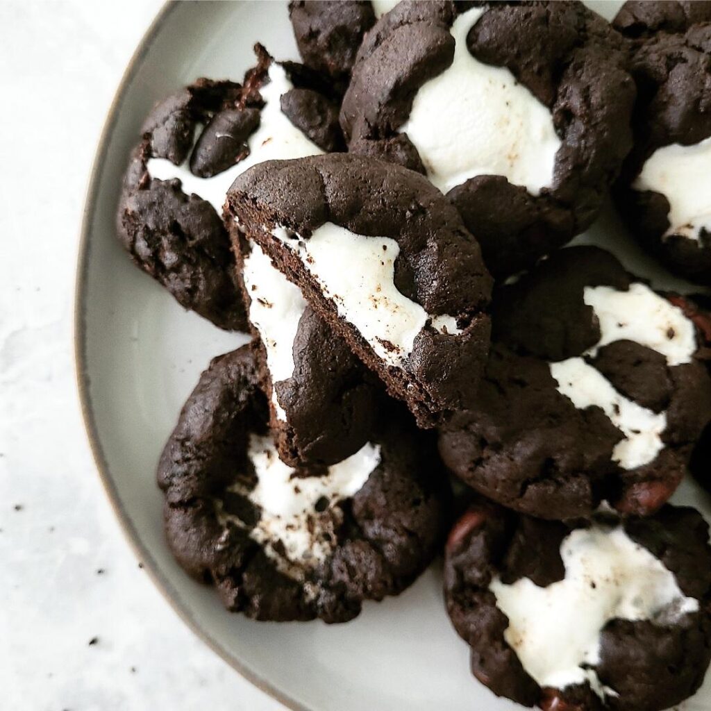 chocolate marshmallow cookies top down view of black and white cookies stacked on a gray plate on a marble surface one cookie is cut in half and piled on top of the others