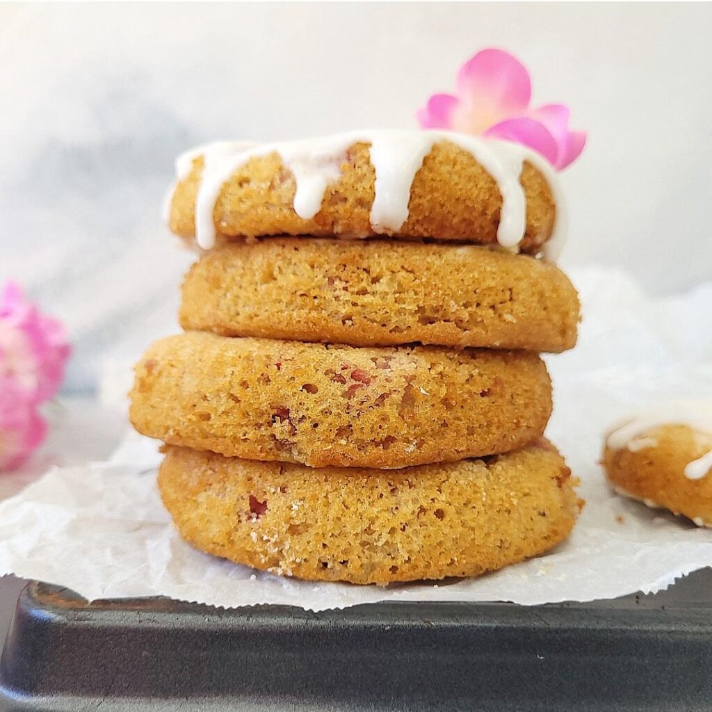 baked strawberry donuts stacked 4 high. top donut on the stack is dripping with a white glaze and garnished with a pink flower.