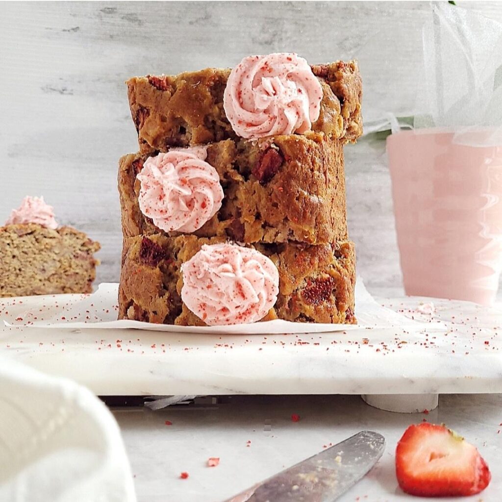 side view of strawberry banana bread cut into three thick slices and stacked on top of each other. each slice is piped with a swirl of strawberry buttercream frosting. 