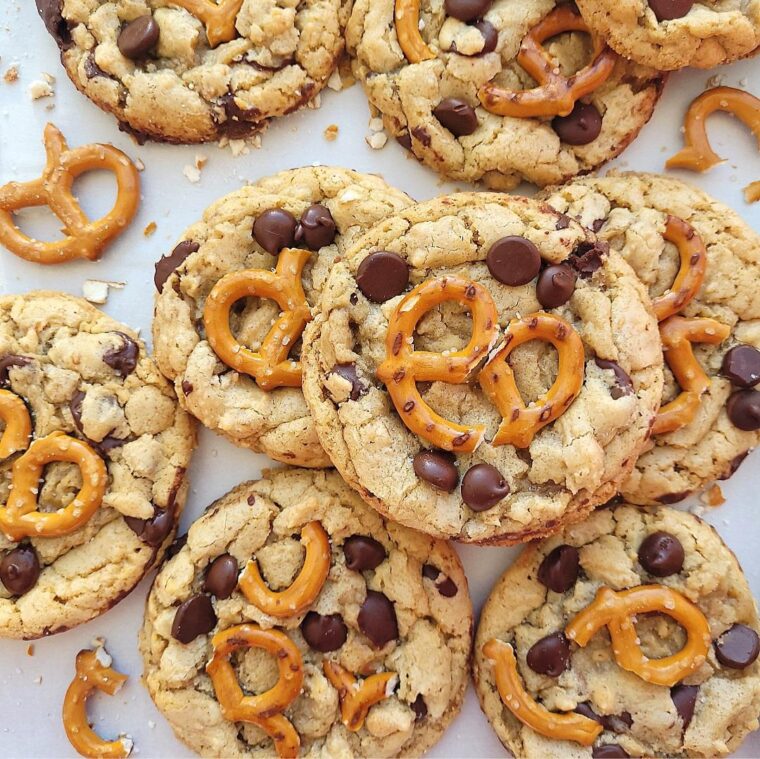 pile of chocolate chip pretzel cookies. top down view of cookies on a white surface styled with broken pretzels and pretzel crumbs.