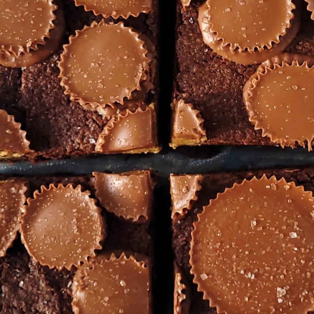 reeses peanut butter cup brownies. top down close up view of 4 cut brownie squares each topped with whole peanut butter cups. peanut butter cups have sea salt on them for texture.