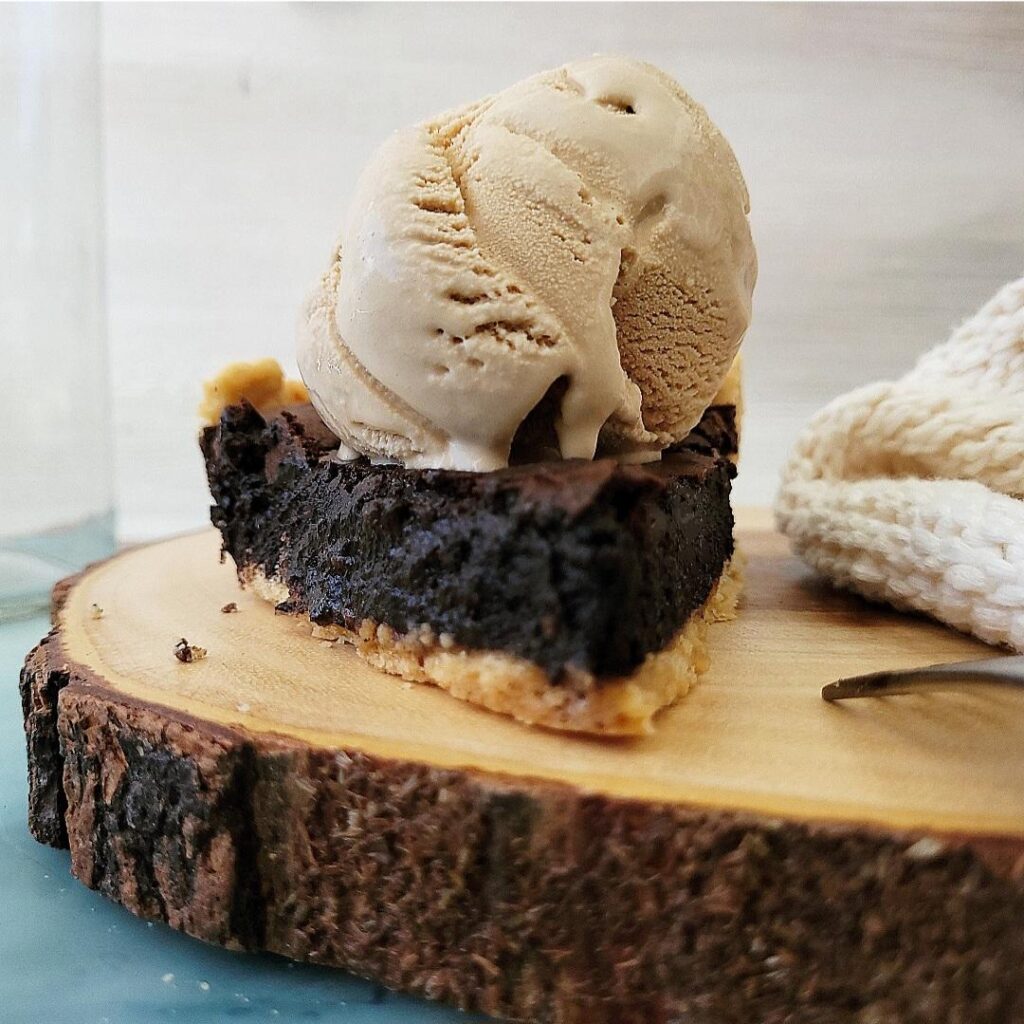 chocolate chess pie slice on a wooden bark charger. slice has a giant scoop of coffee ice cream on top. 