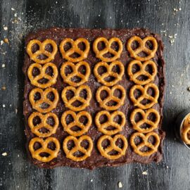 salted pretzel nutella fudge. top down view of fudge on a black surface. fudge is uncut and topped with rows and columns of salted mini pretzels.