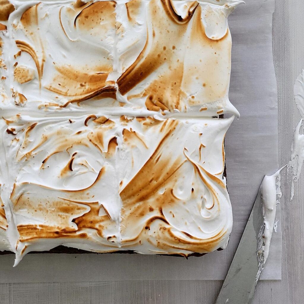 sweet potato cake with marshmallow frosting that has been toasted with a blow torch. top down image styled with a knife that has marshmallow meringue on the tip.