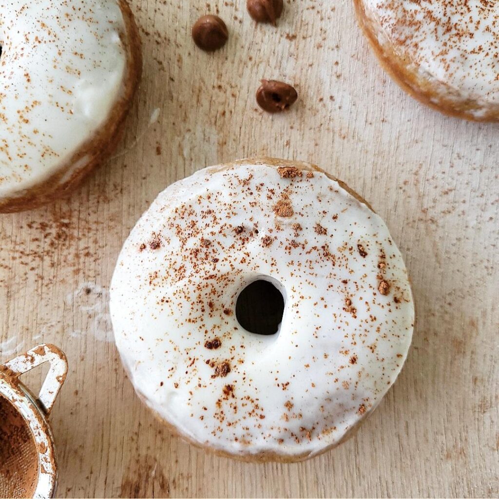 baked banana donuts with condensed milk frosting dusted with cocoa powder. top down view of one donut on a pale wood surface. 