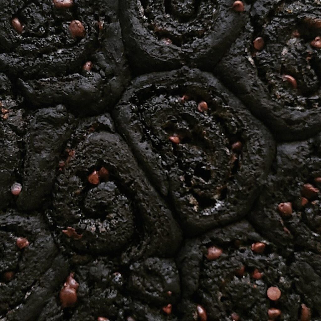 dark chocolate cinnamon rolls. zoomed in view of rolls without frosting. rolls are jet black from black cocoa and filled with mini chocolate chips. 