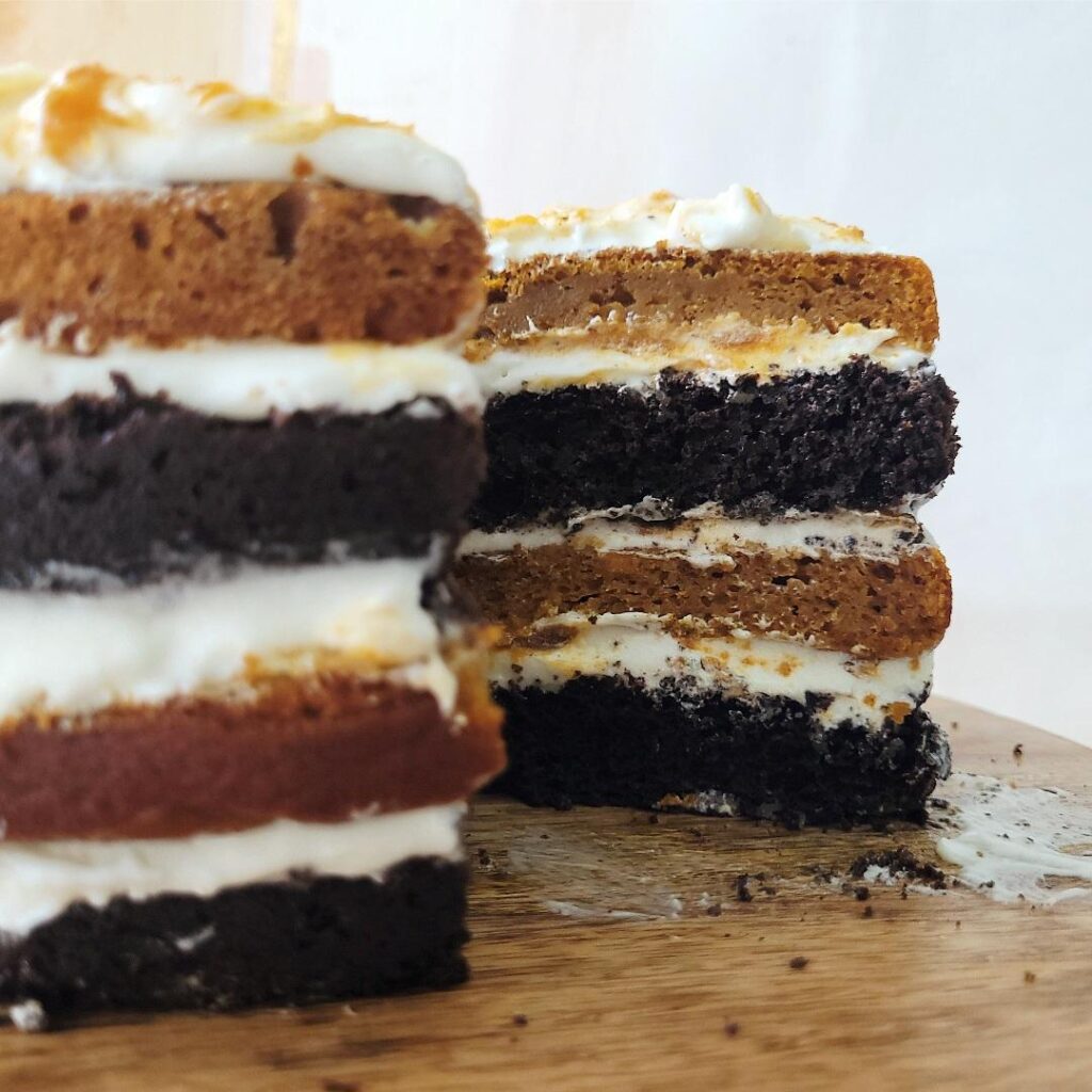 chocolate pumpkin layer cake with cream cheese frosting. alternating layers of chocolate cake and pumpkin cake with white cream cheese frosting in between. side view of cake with one slice protruding so you can see the inner crumb layers. 