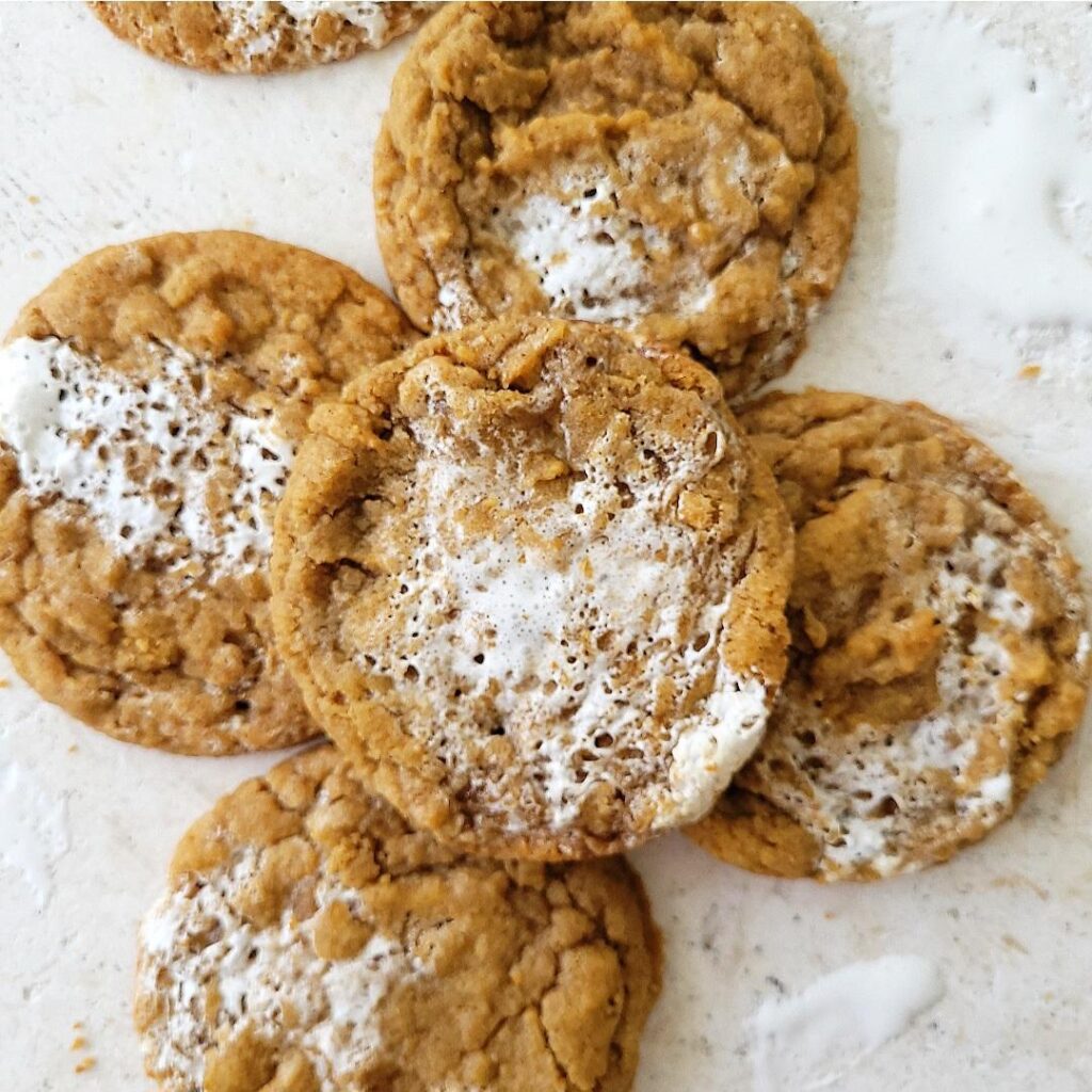 pumpkin marshmallow cookies. top down view of 4 pumpkin cookies swirled with marshmallow cream on a white marble background. 