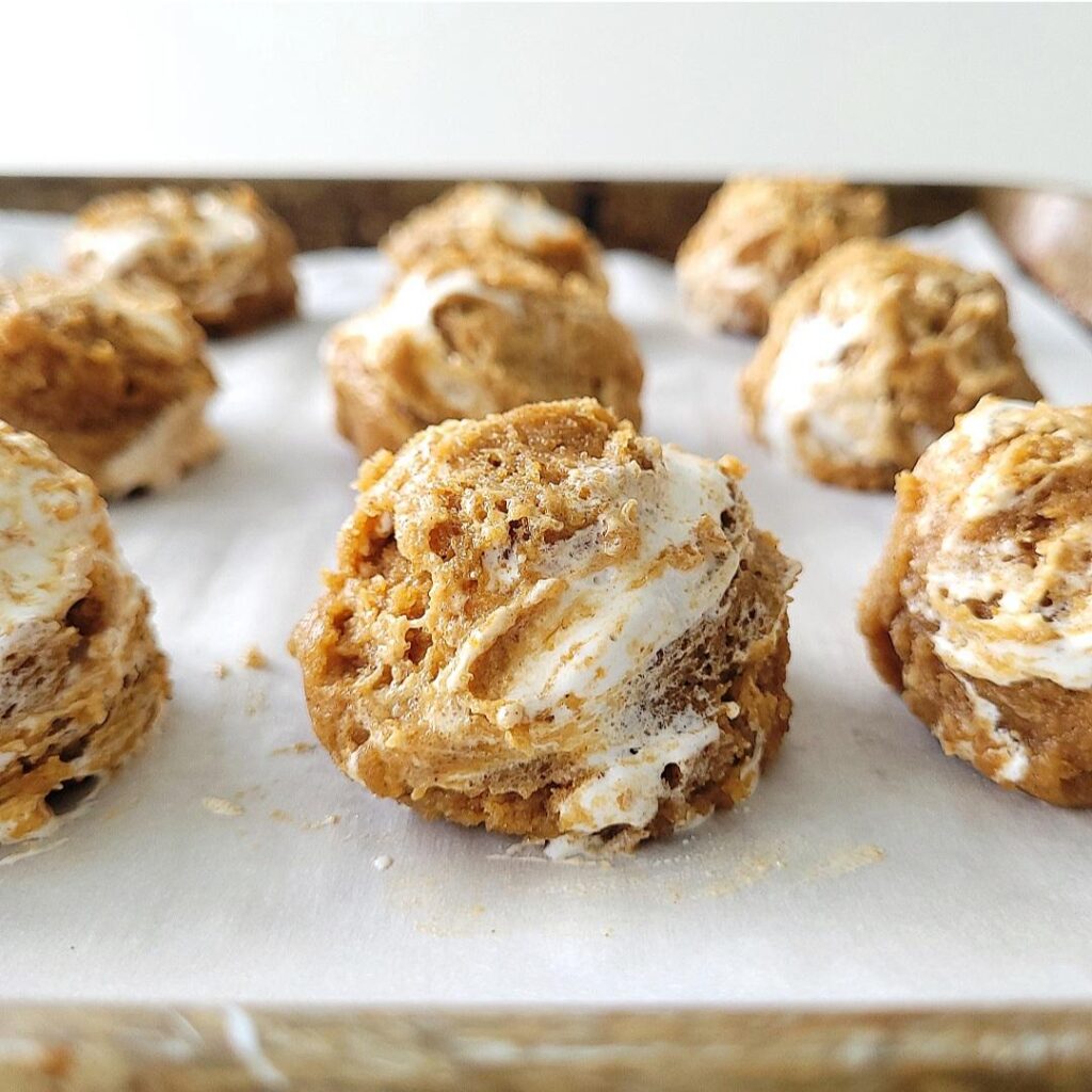 pumpkin marshmallow cookies. close up view of cookie dough scooped into balls and placed on a baking sheet lined with parchment so you can see the swirls of jet puffed marshmallow creme in the pumpkin cookie dough