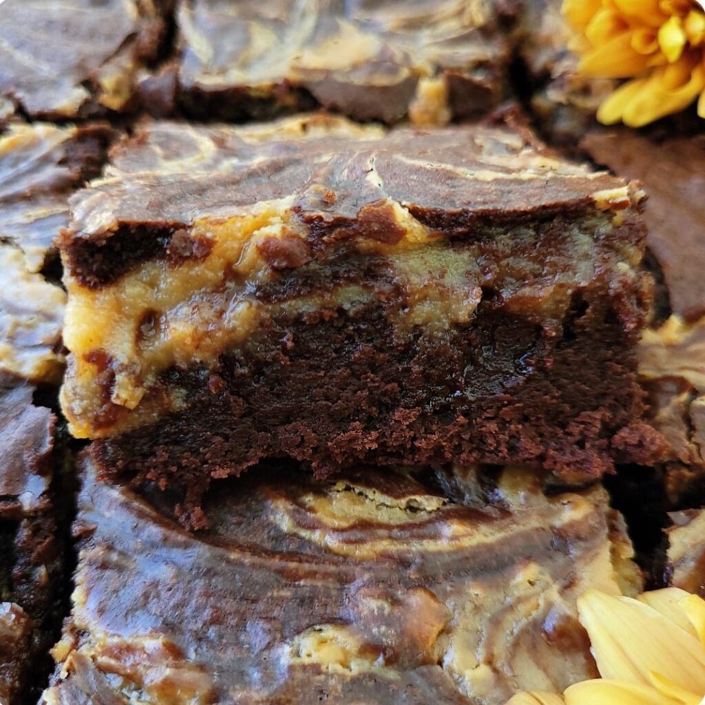 caramel brownies cut into slices. close up view of one brownie diagonally resting on another slice so you can see the gooey caramel layer mixed in with the brownie layer. 