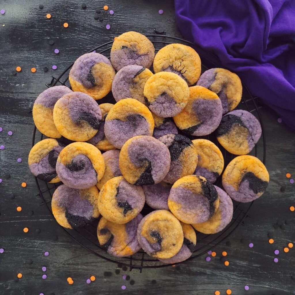 hocus pocus cookies. top down view of these orange purple and black swirled halloween sugar cookies on a black background