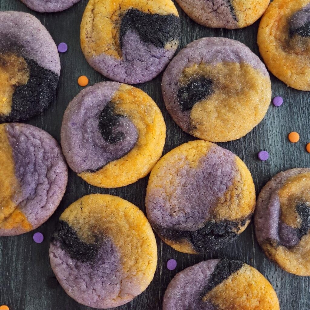hocus pocus cookies. top down view of halloween sugar cookies swirled with purple, black and purple on a black surface.  halloween cookies are laying flat in a random pattern. 